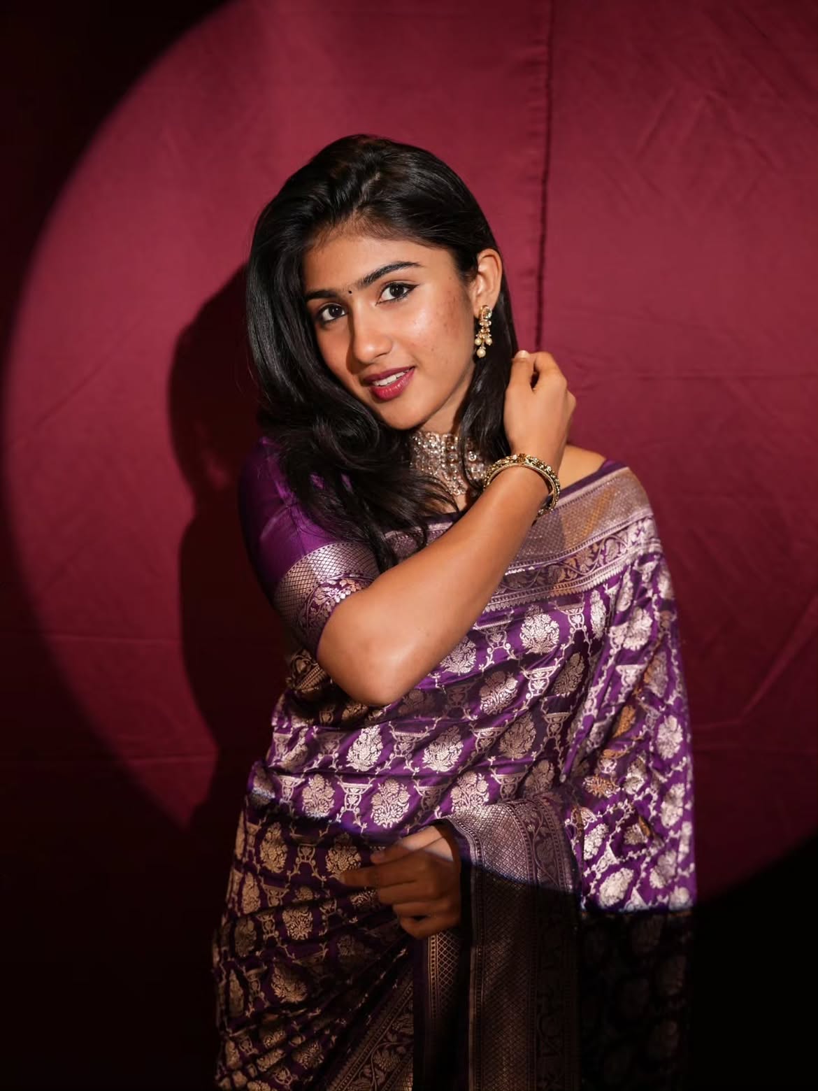 Riya Shibu in a purple sari against a deep burgundy backdrop